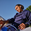 Person wearing a blue hoodie sitting outdoors, looking at a magazine.